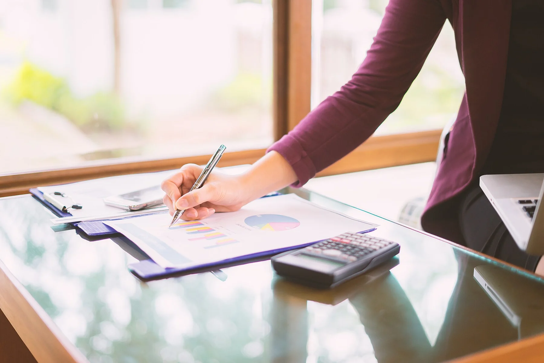 Printed quote figures being checked with a pen beside a calculator and laptop